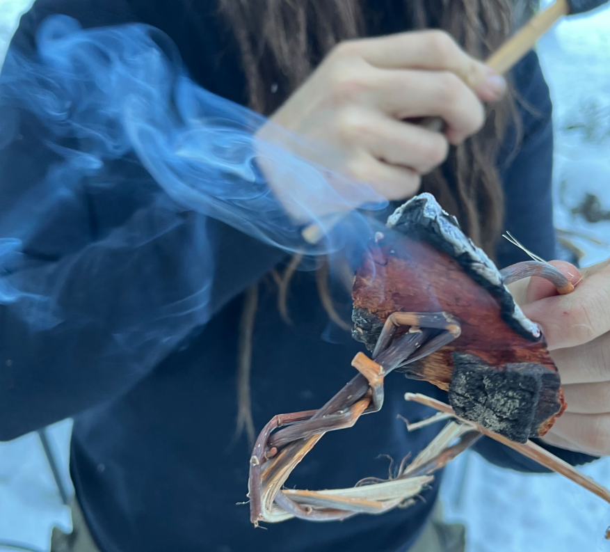 person holds smoking bit of bark and braided twigs
